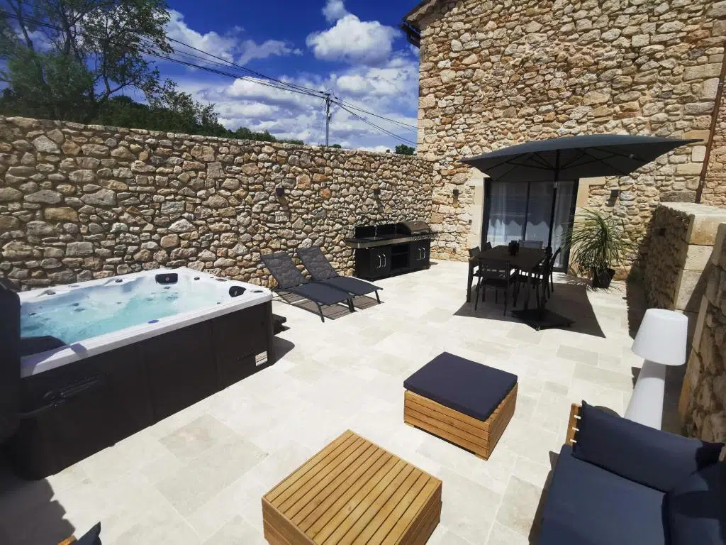 Espace extérieur du Domaine du Grand Cru avec jacuzzi, espace solarium et table de jardin ombragée,